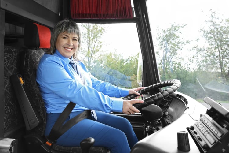 a bus driver smiles in greeting from the driver seat of a charter bus